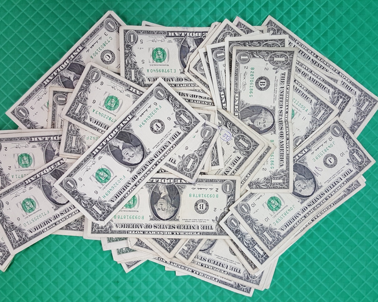 Много купюр в один доллар на зеленой поверхности