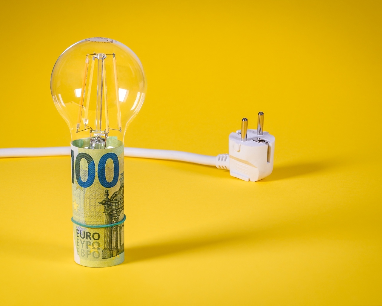 Лампочка с деньгами и розеткой на желтом фоне