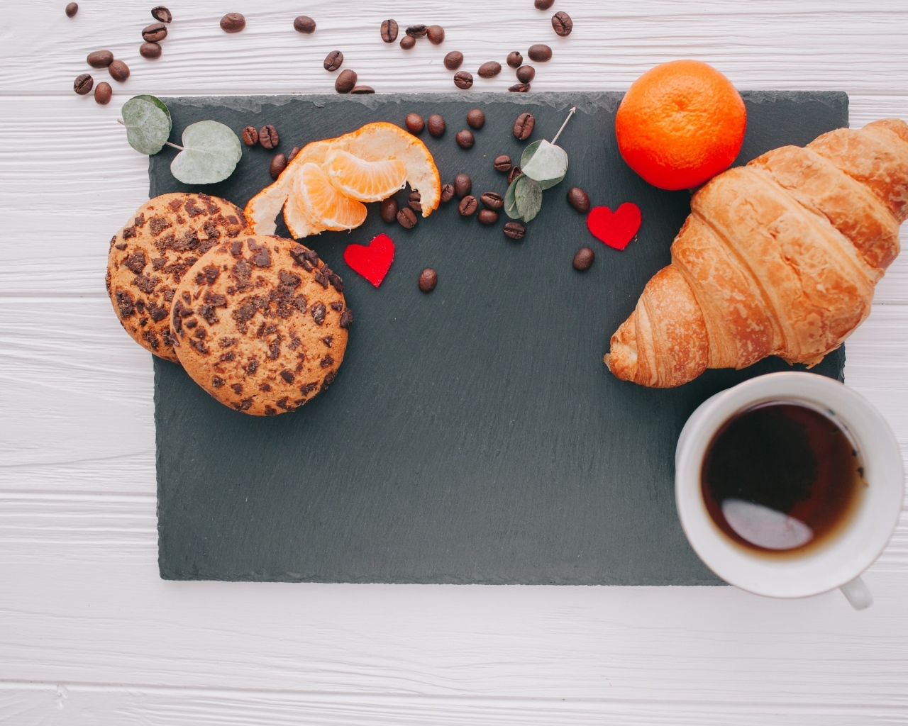 Круассан на столе с печенье, чашкой кофе и мандарином