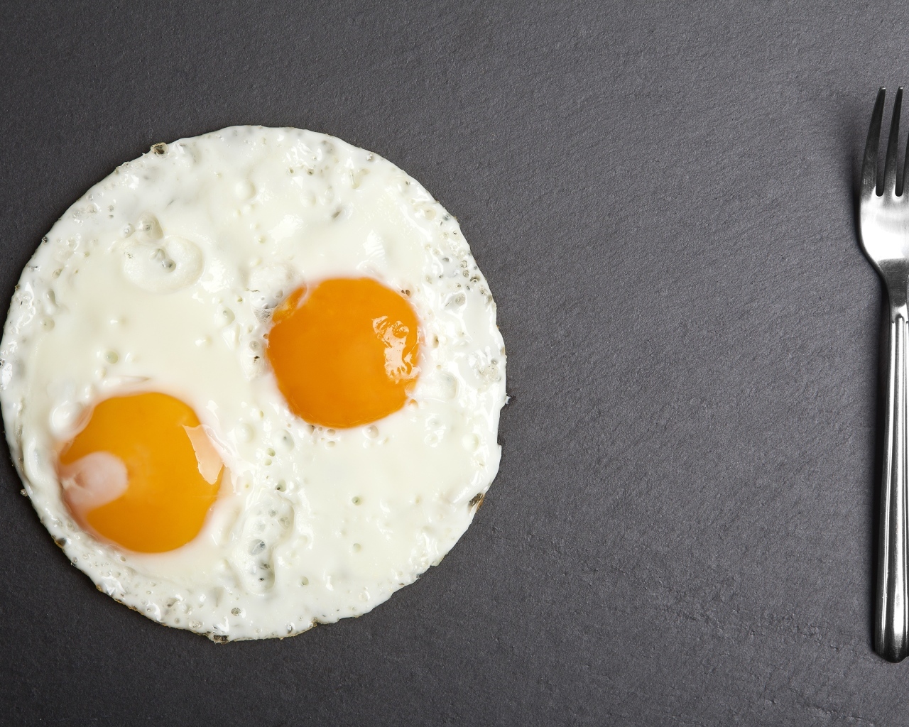 Яичница глазунья с вилкой на сером столе