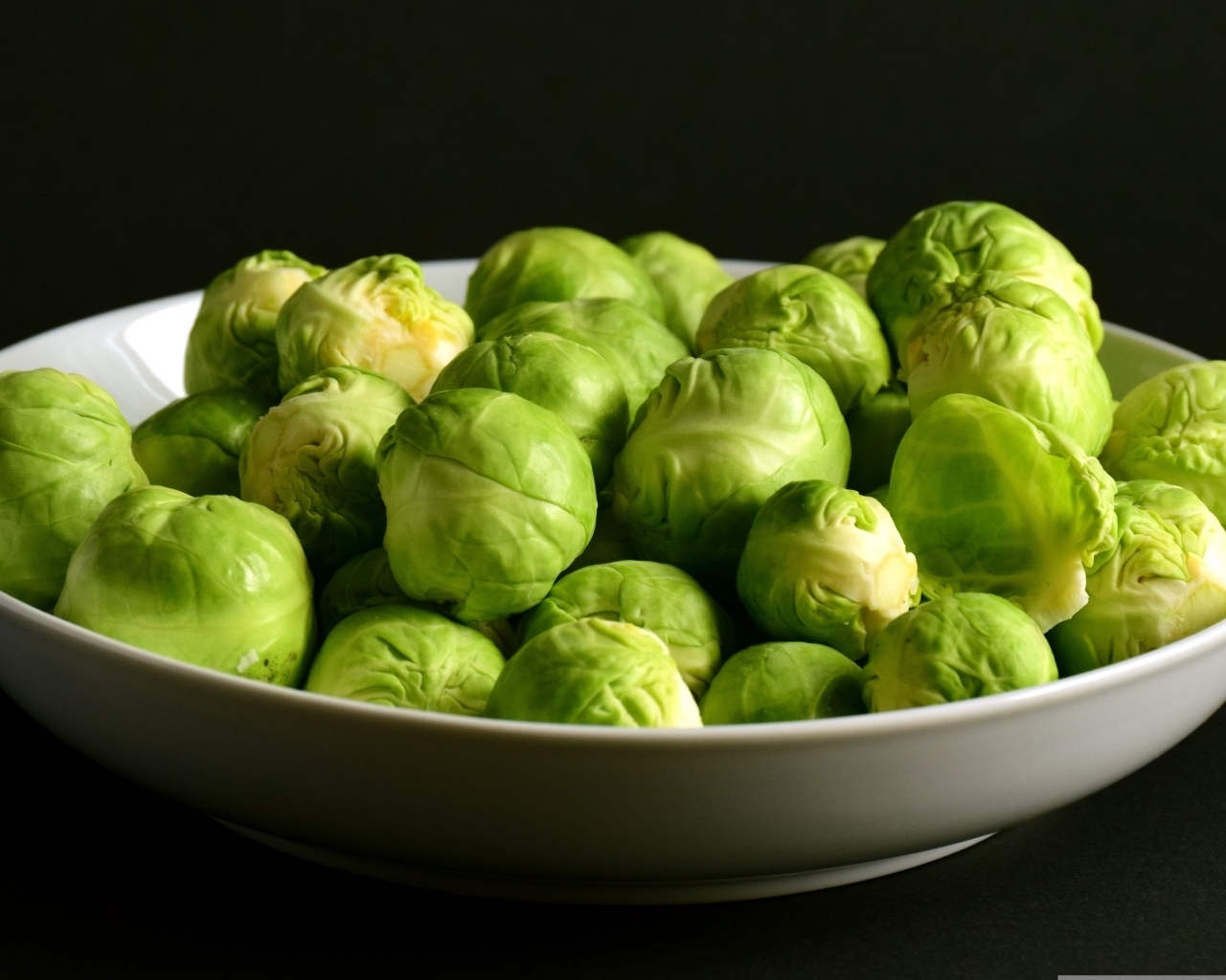 Зеленая брюссельская капуста в тарелке на черном фоне