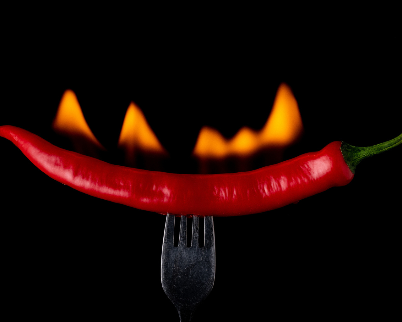 Жгучий красный перец на вилке на черном фоне