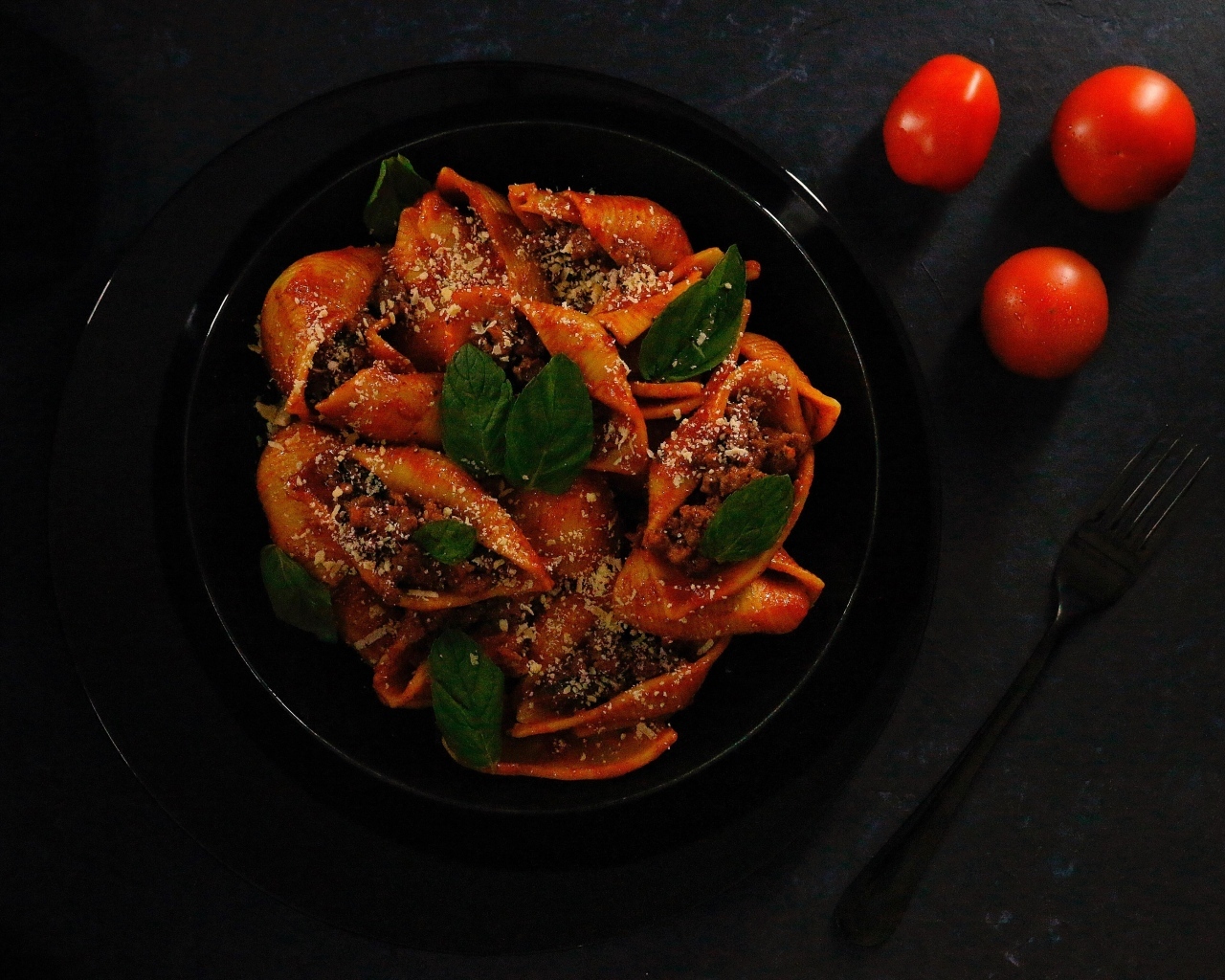 Большие макароны с фаршем в черной тарелке