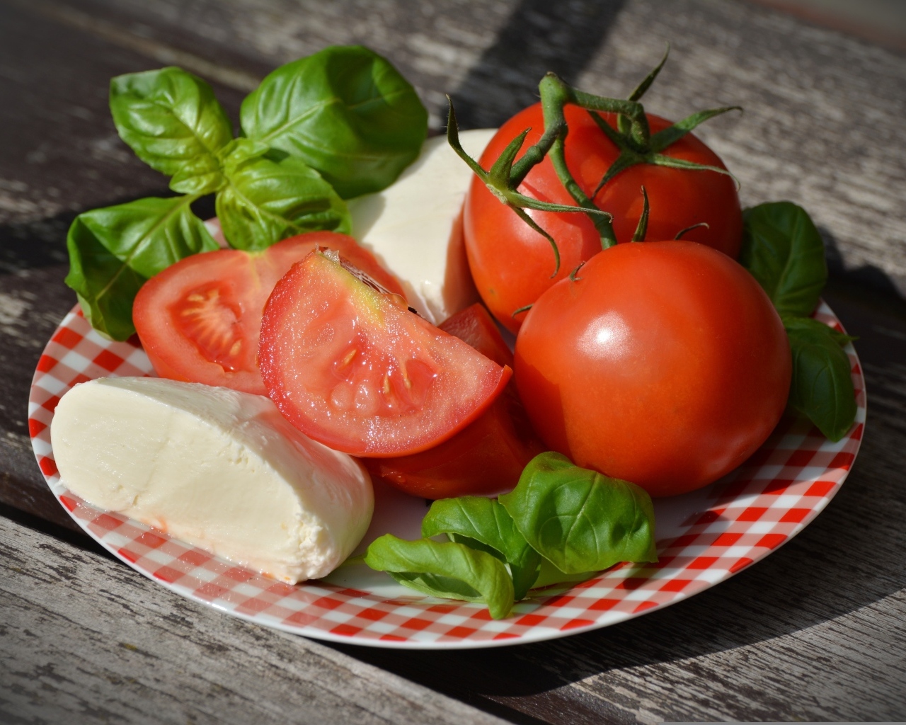 Красные помидоры с сыром и базиликом на тарелке