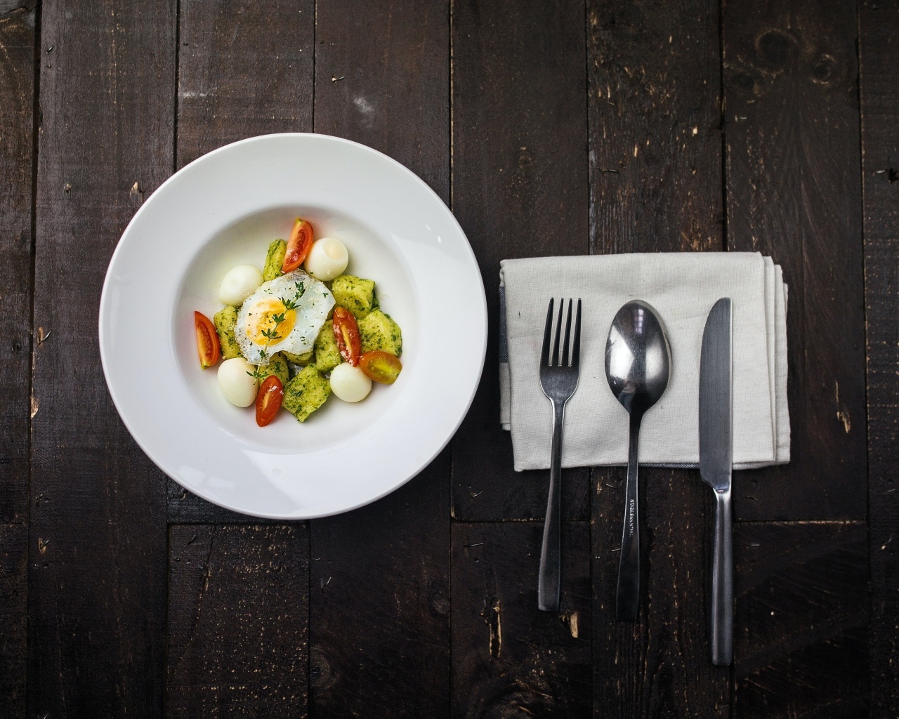 Яичница с овощами в белой тарелке на столе со столовыми приборами