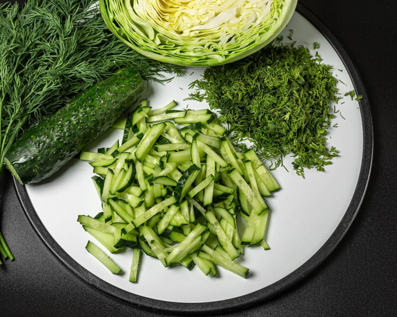 Нарезанные огурцы на столе с капустой и укропом