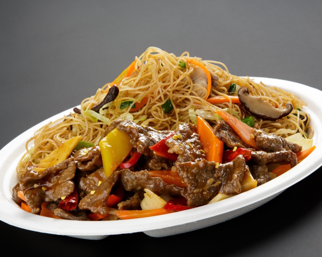 Острая лапша с грибами на белой тарелке на сером фоне