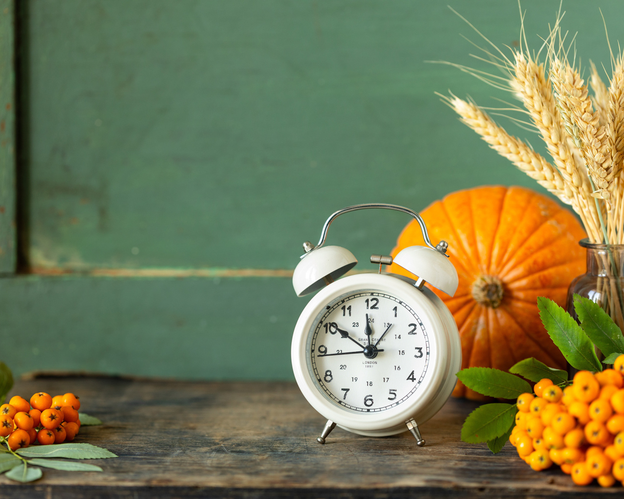 Будильник на столе с тыквой и ягодами рябины