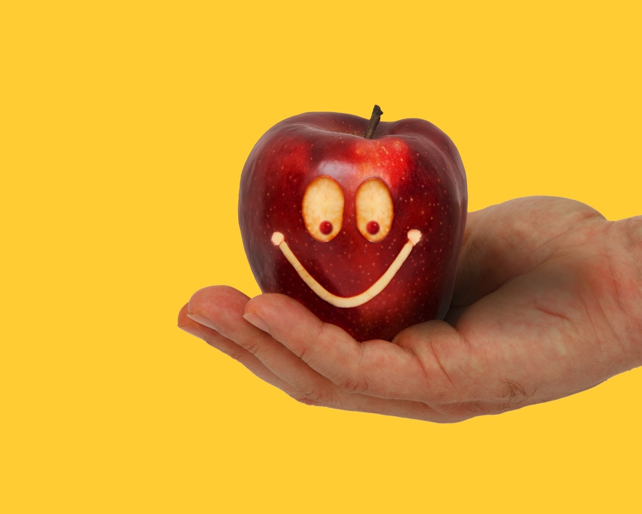 Яблоко на ладони на желтом фоне