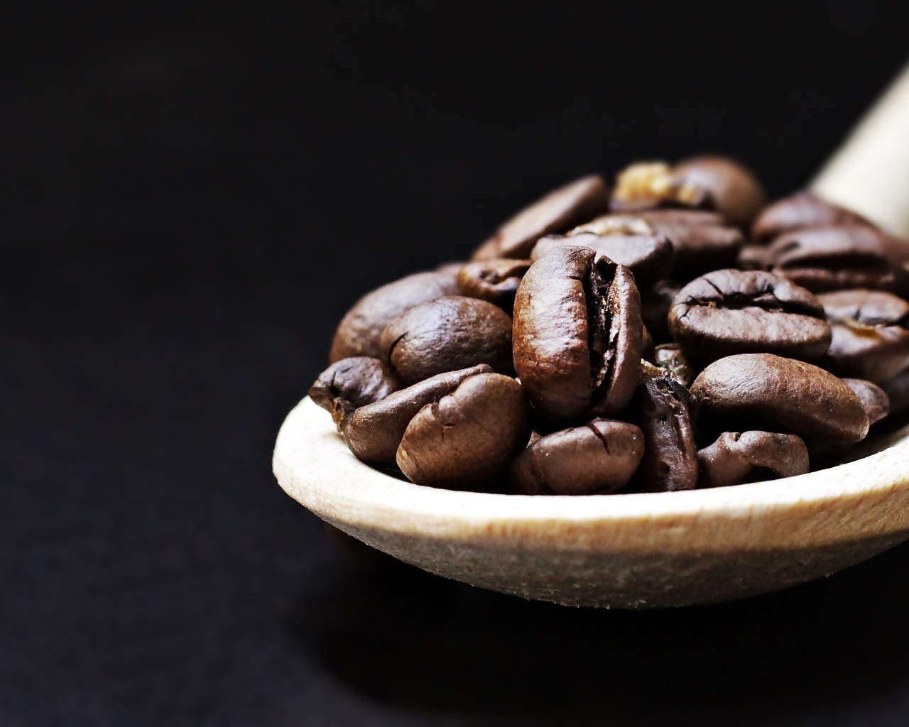Зерна кофе на деревянной ложке на черном фоне
