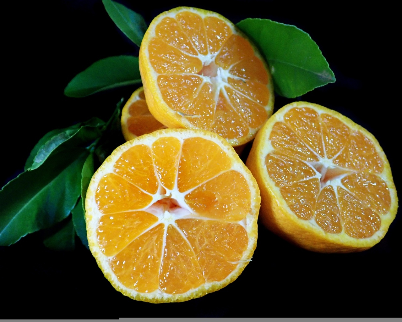 Половинки мандарина с зелеными листьями на черном фоне