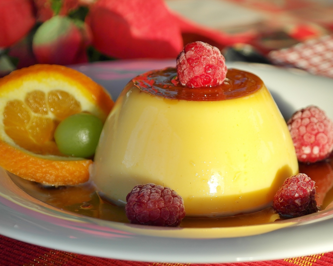 Желе в карамели на тарелке с ягодами малины и апельсином