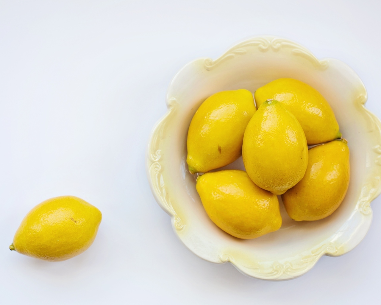 Крупные желтые лимоны в тарелке на белом фоне