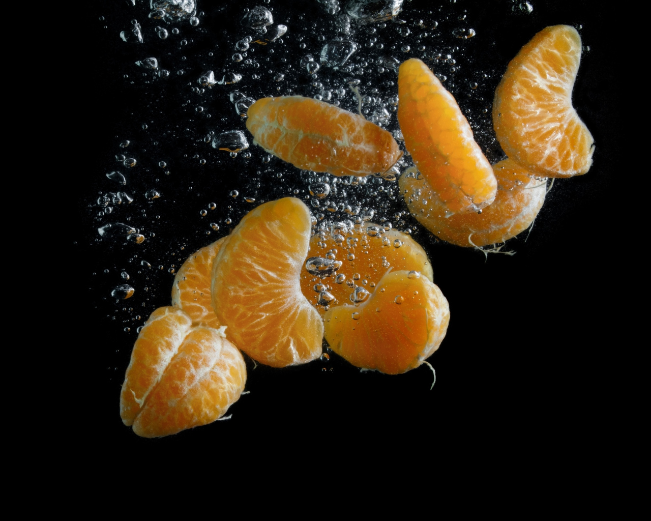Дольки мандарина в воде на черном фоне