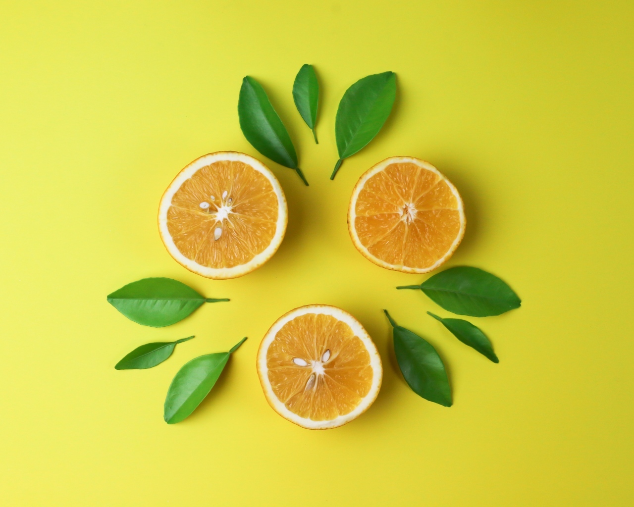 Половинки апельсина с зелеными листьями на желтом фоне
