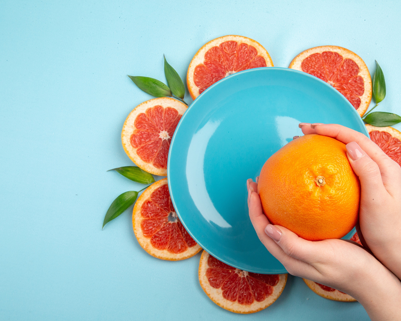 Апельсин в руках девушки на голубом фоне с тарелкой