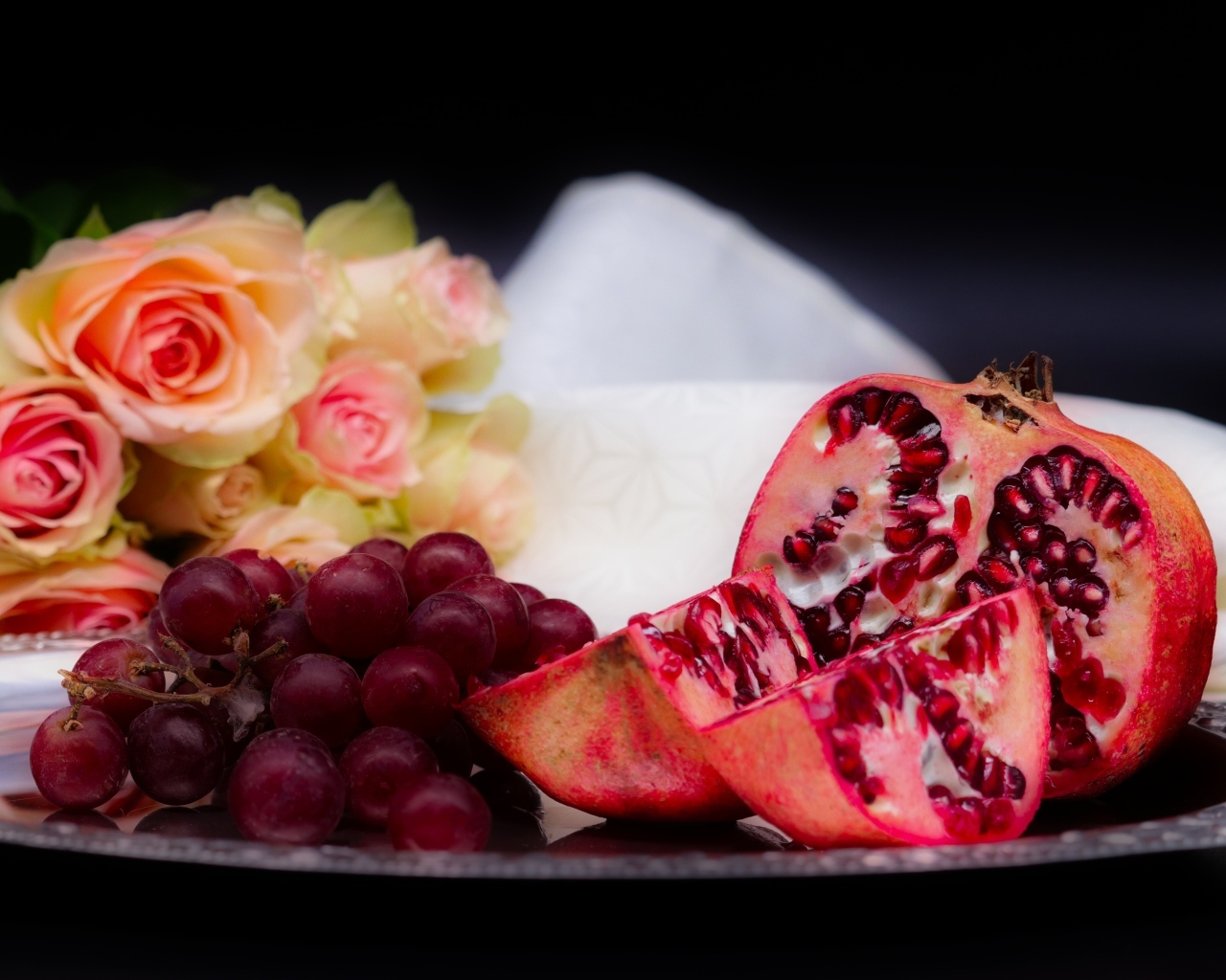 Гранат с виноградом на столе с букетом роз 