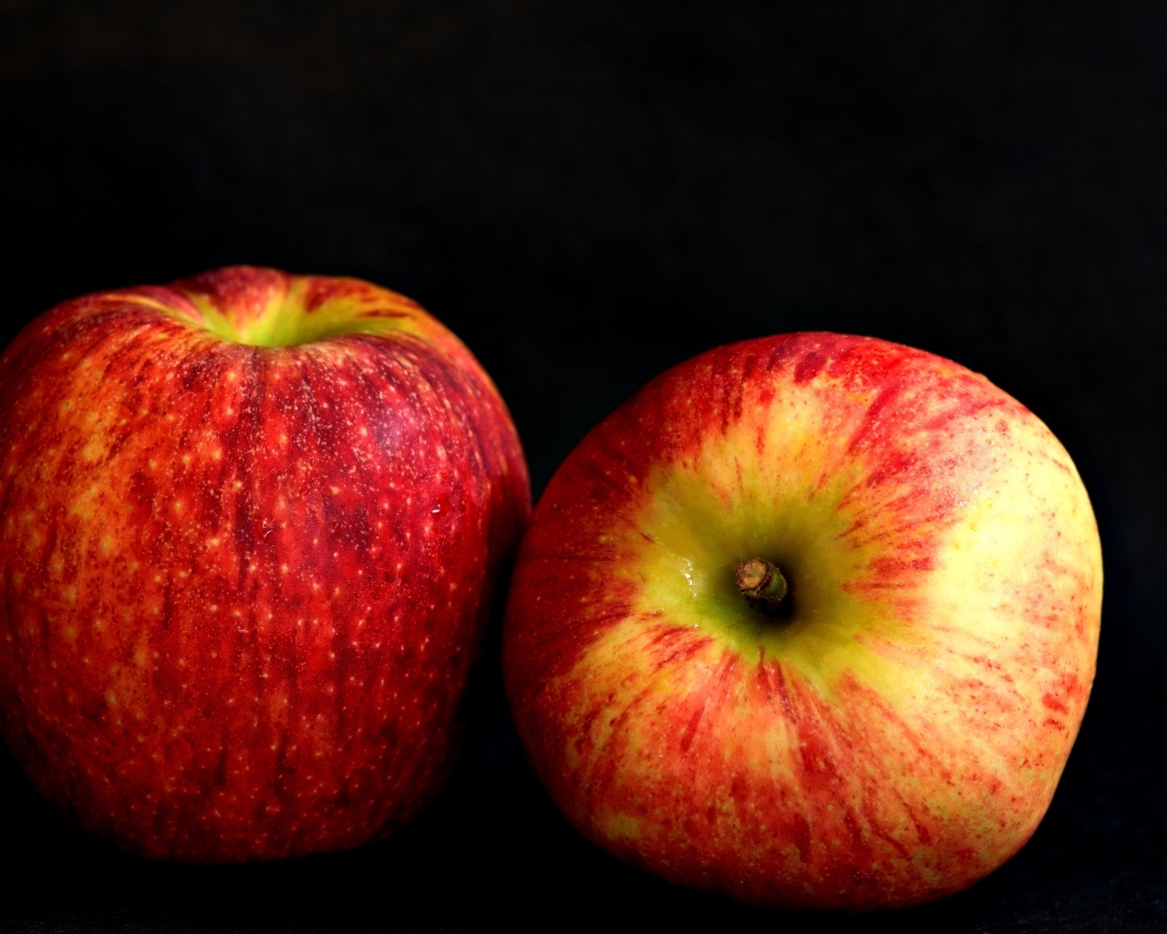 Два больших спелых красных яблока на черном фоне