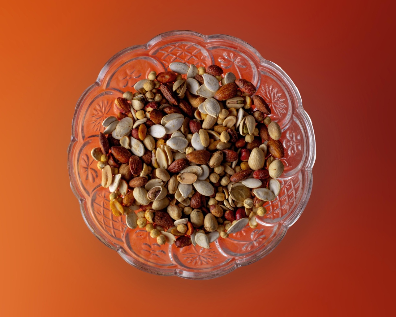 Разные орехи в стеклянной посуде на оранжевом фоне