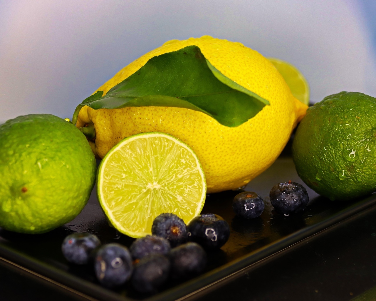 Желтый лимон на тарелке с лаймом и ягодами черники 