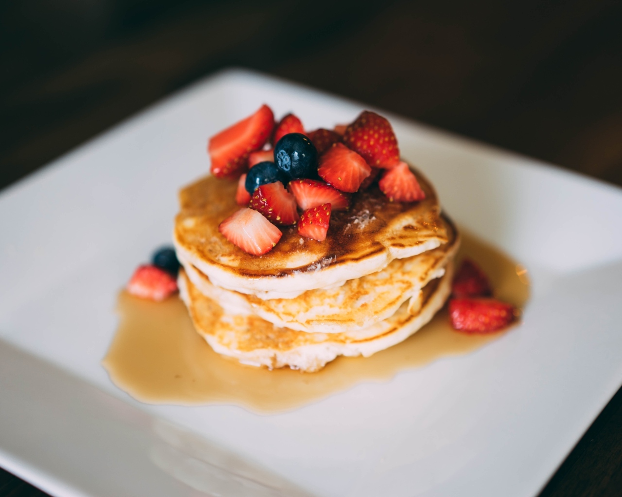 Оладьи с кусочками клубники, медом и черникой на тарелке