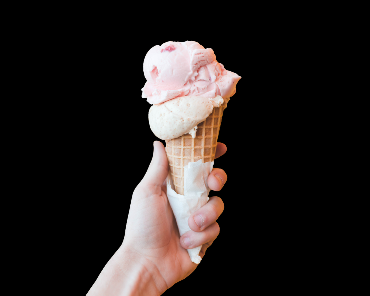 Розовое мороженое в рожке в руке на черном фоне