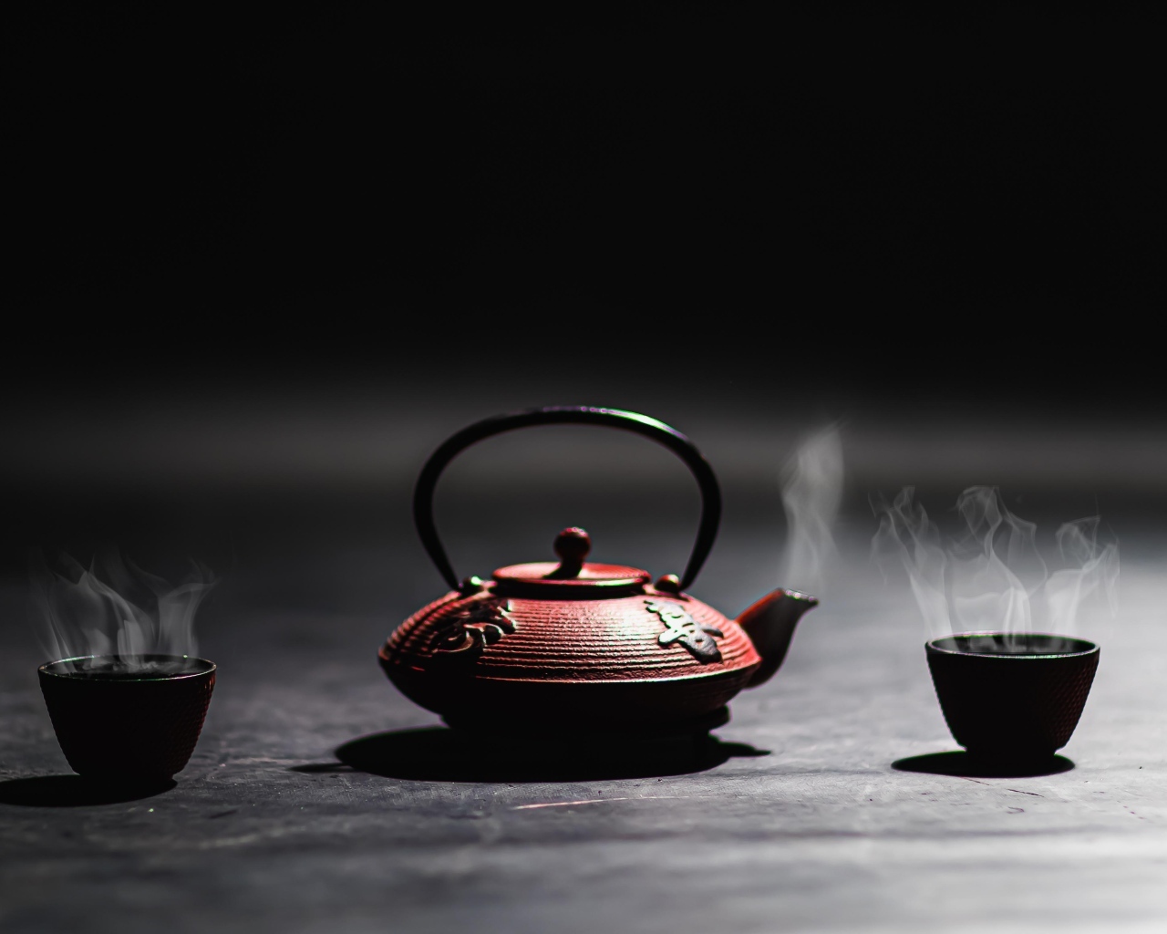 Чайник с горячим чаем на черном фоне