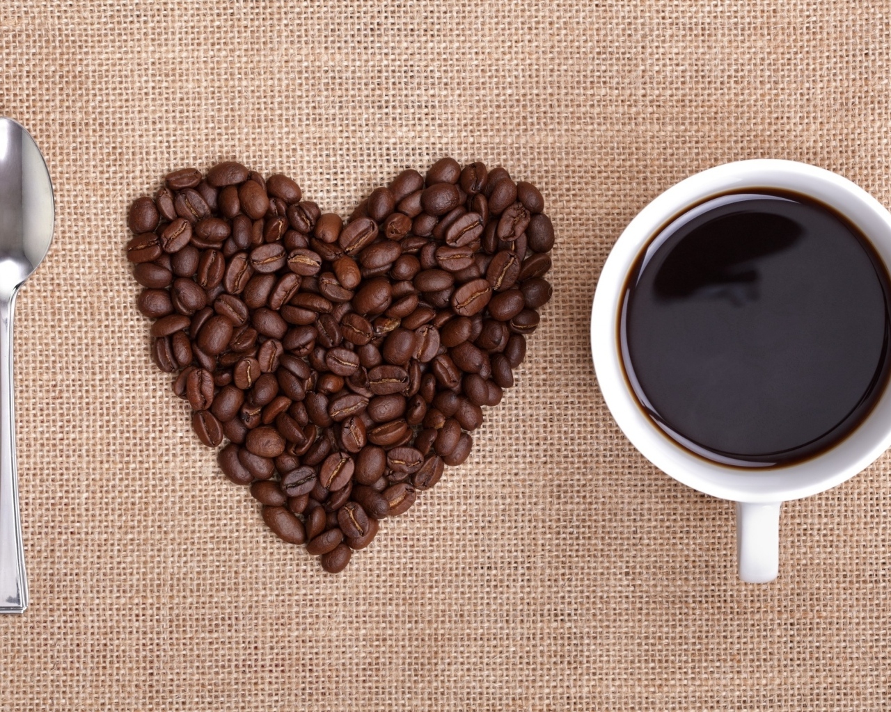Ложка, сердце из кофейных зерен и белая кружка на столе