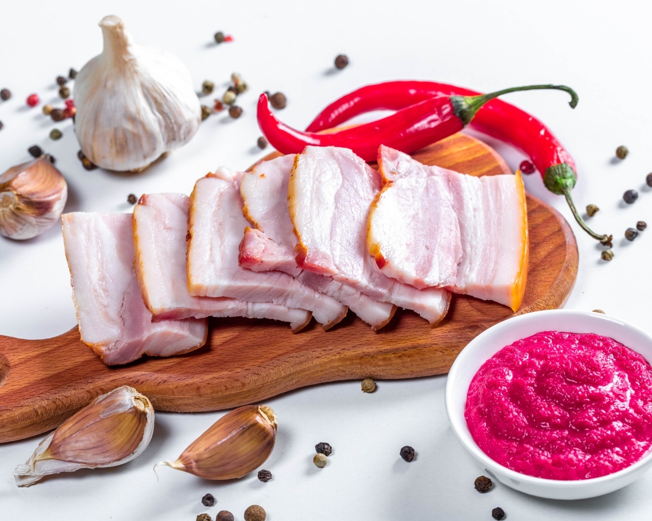 Нарезанное сало на столе с чесноком, хреном и красным перцем