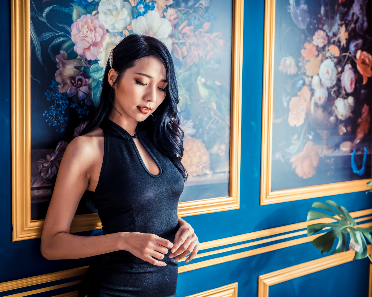 Красивая девушка азиатка в черном платье стоит у картины 