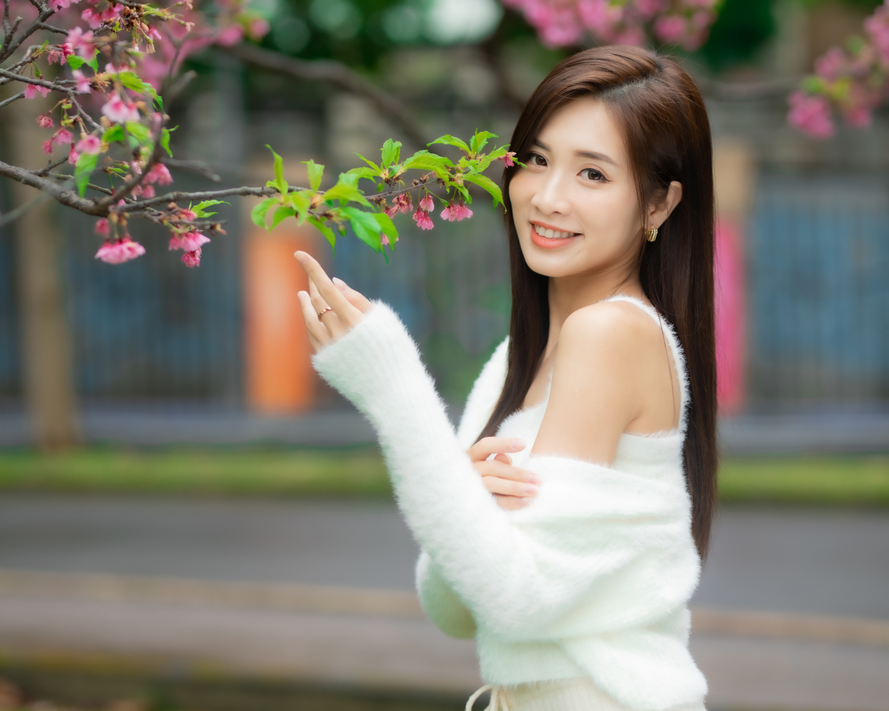 Красивая азиатка в белом свитере стоит у ветки дерева