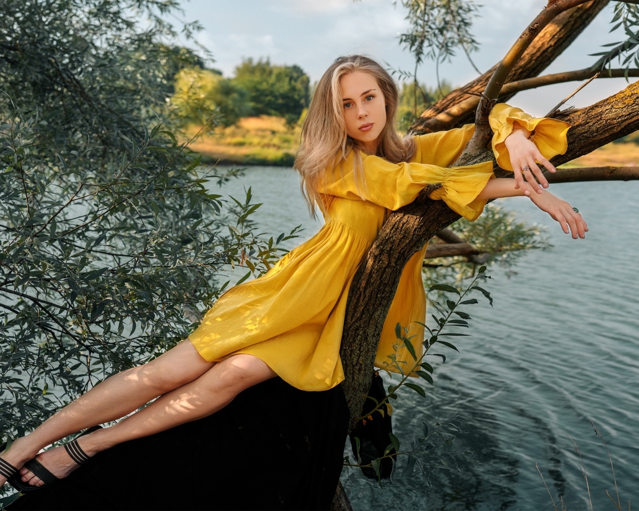 Красивая девушка в желтом платье лежит на дереве у воды