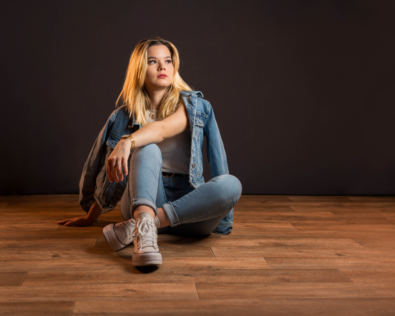 Девушка в джинсовом костюме сидит на полу