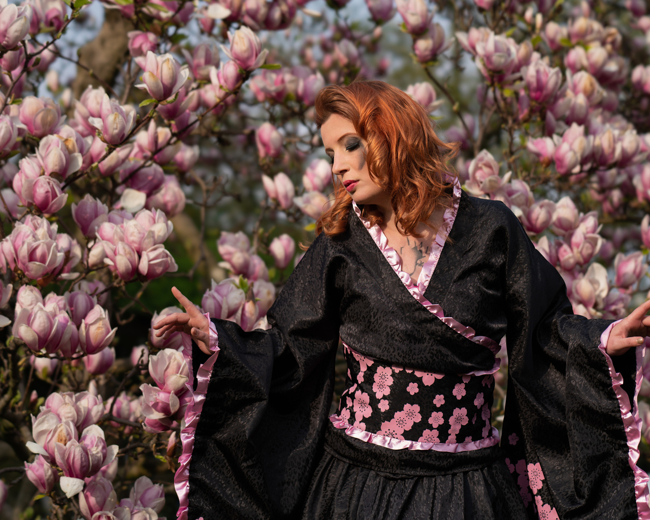 Девушка в кимоно стоит у куста с цветами магнолии