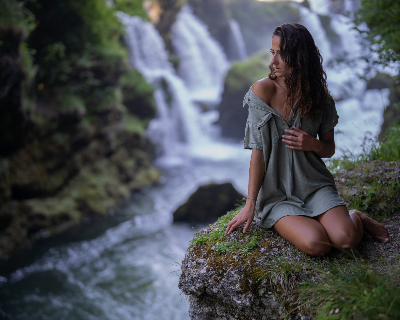 Девушка в рубашке сидит у водопада