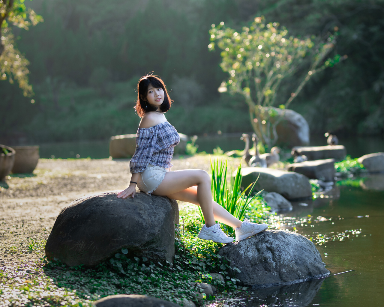 Девушка сидит на большом камне у пруда