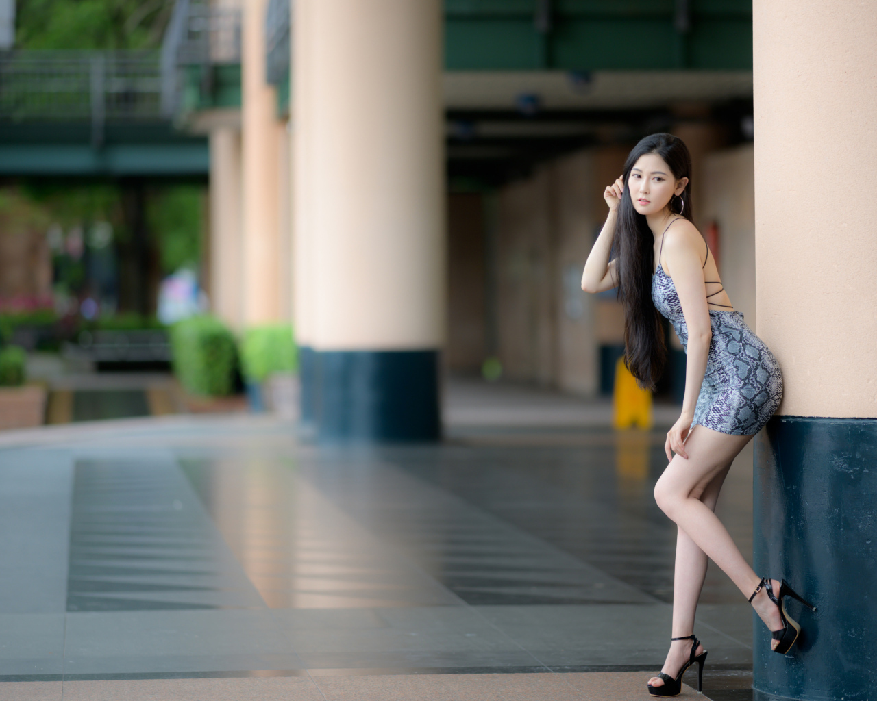 Стройная азиатка в коротком платье  стоит у колонны