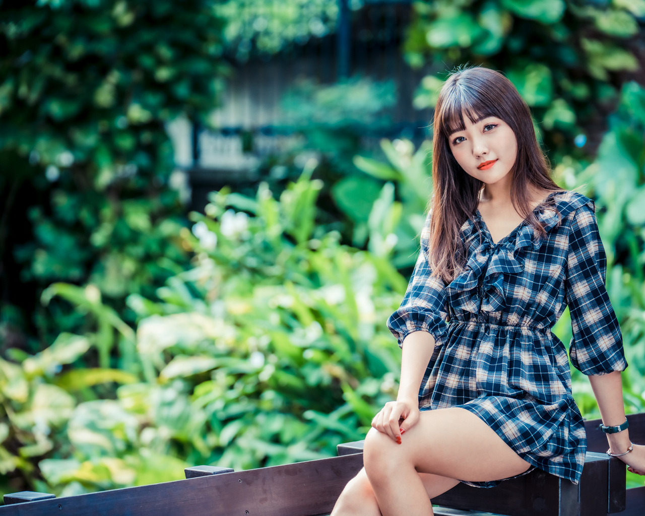 Молодая девушка в клетчатом платье сидит на заборе