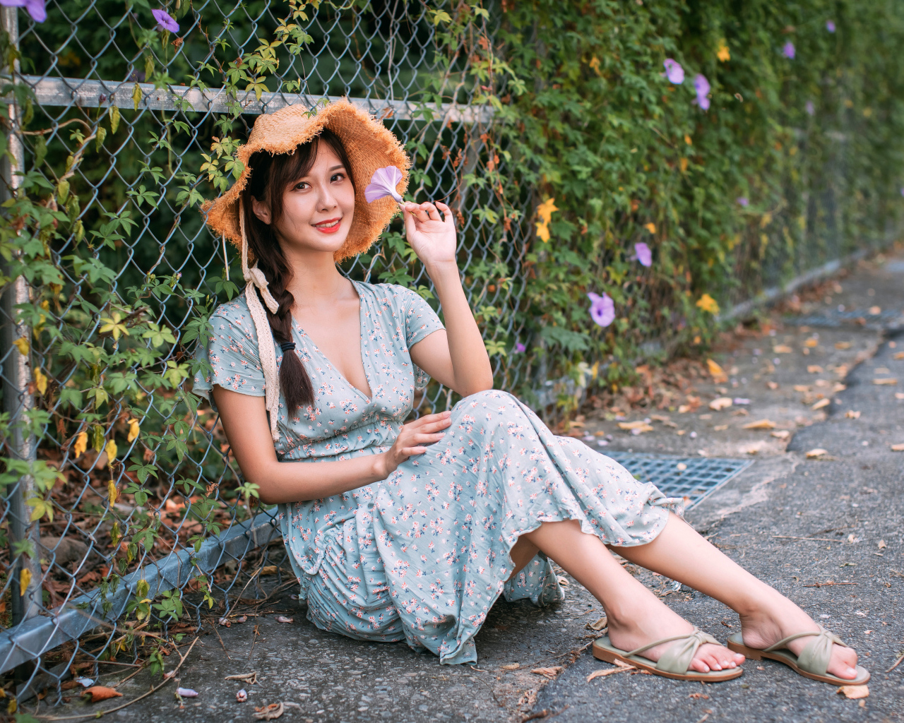 Девушка азиатка в платье сидит у забора