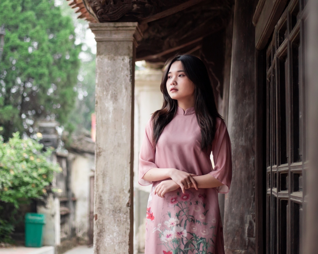 Девушка азиатка в розовом платье стоит у дома