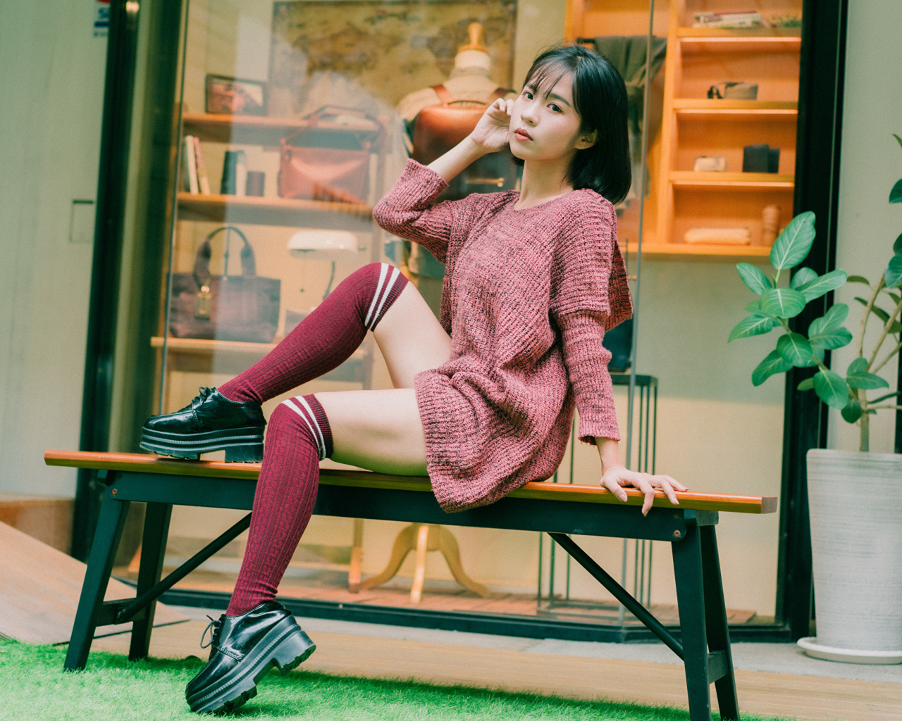 Девушка азиатка в теплом свитере сидит на лавке