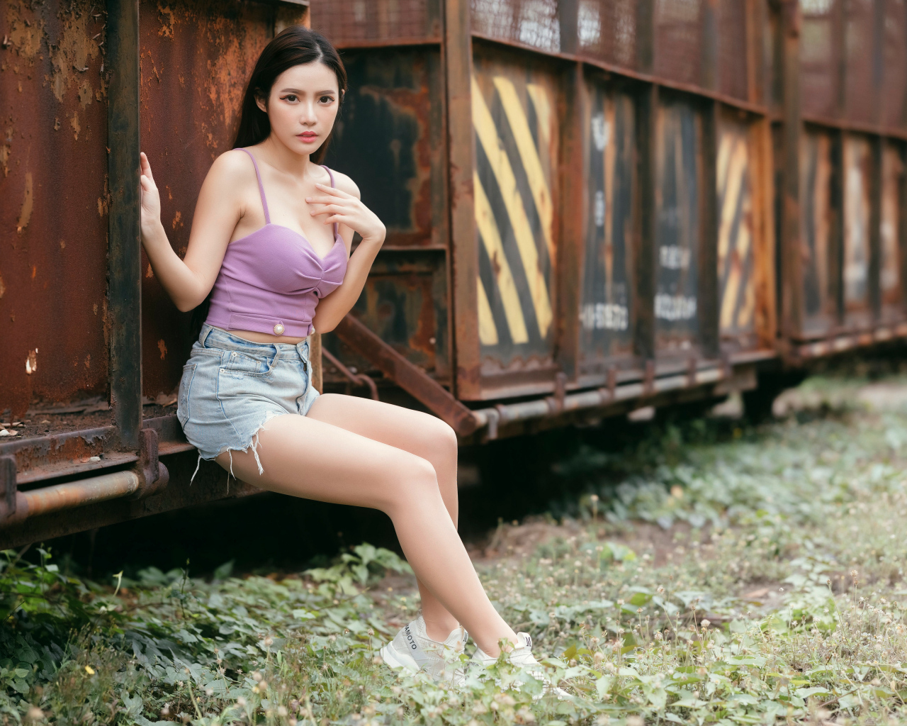 Девушка азиатка сидит у ржавого вагона