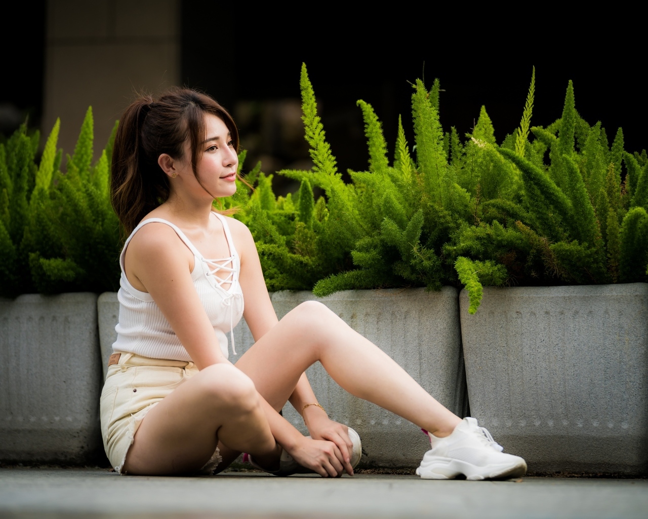 Девушка азиатка сидит на земле у зеленых растений