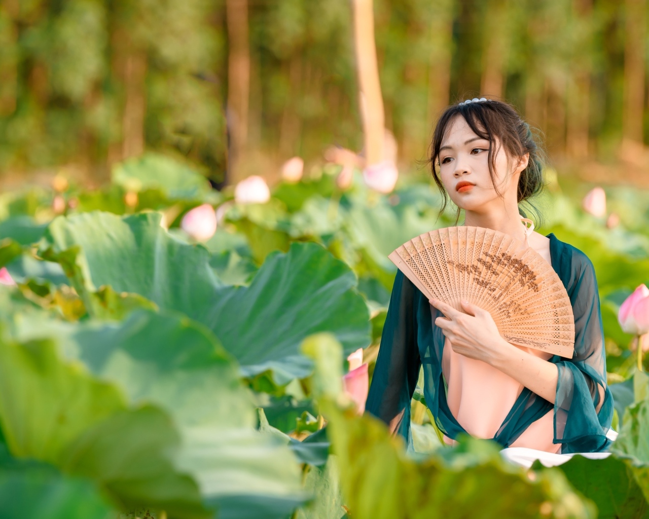 Девушка азиатка с веером в зеленых листьях лотоса