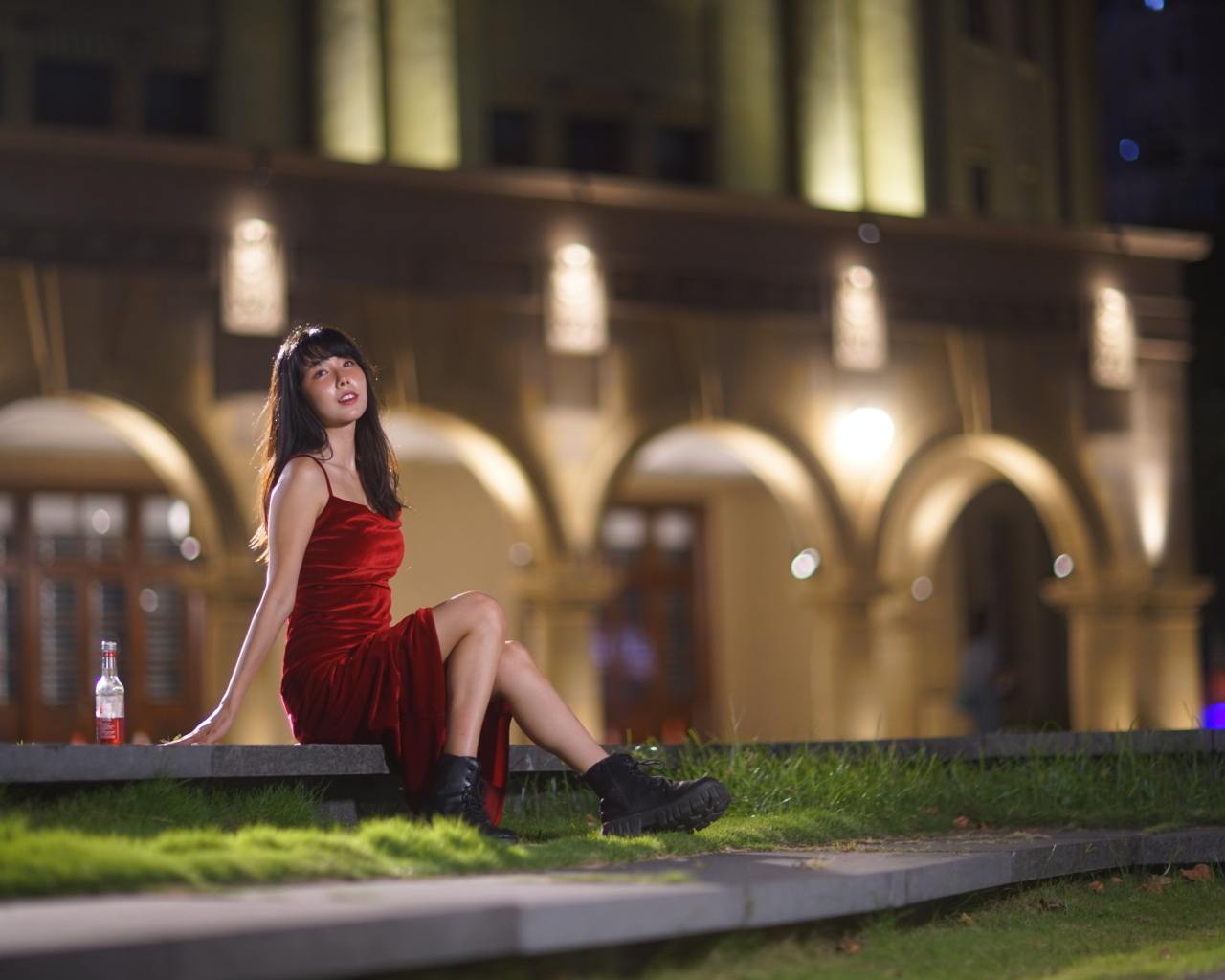 Азиатка в длинном красном платье сидит на ступенях