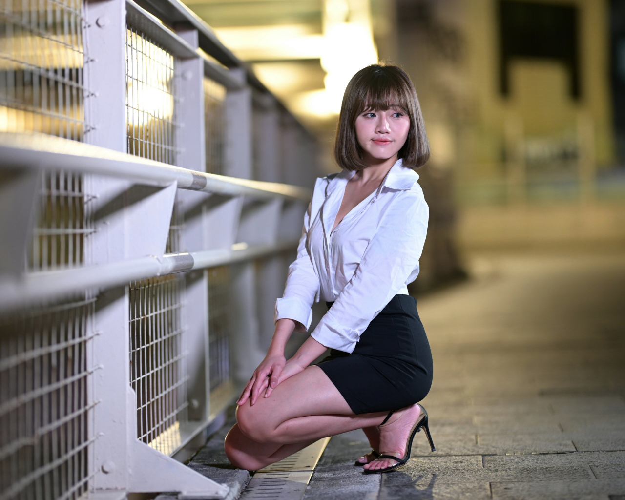 Азиатка в белой блузке и черной юбке сидит на корточках