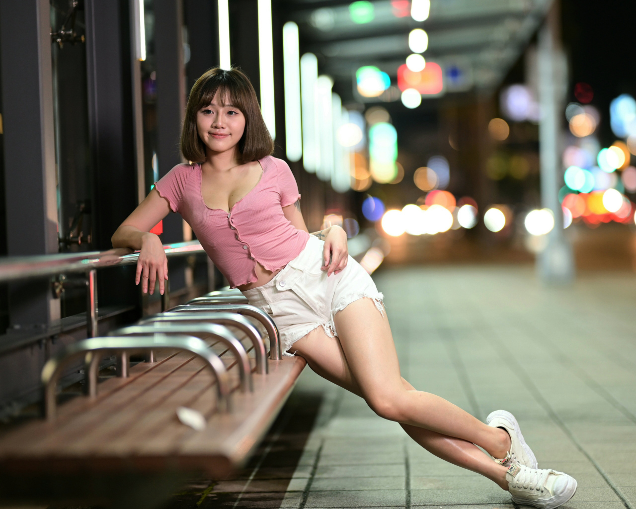 Азиатка в коротких белых шортах сидит на остановке