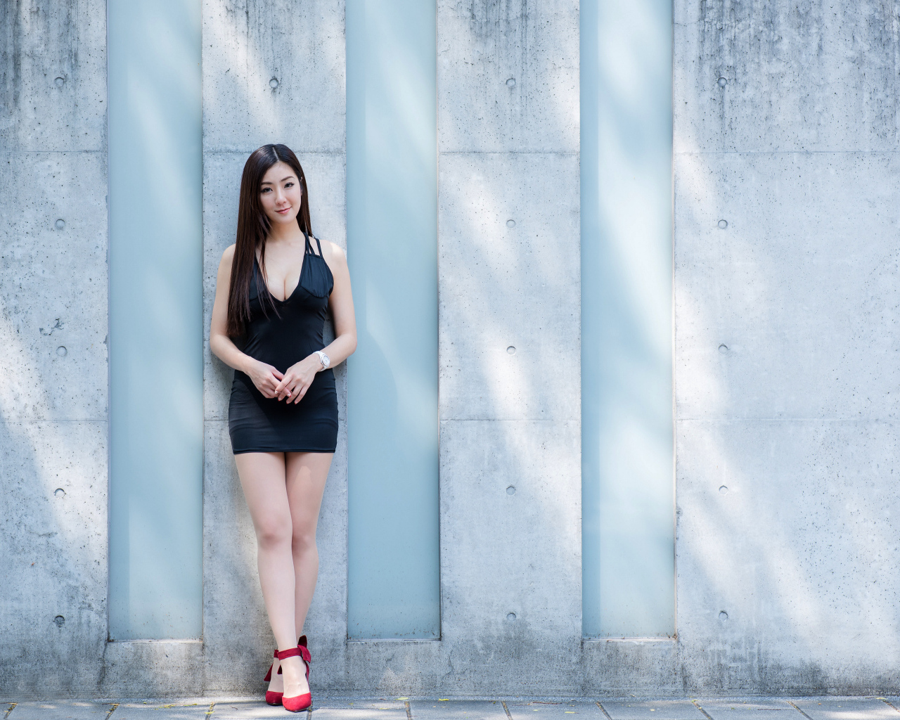 Красивая азиатка в коротком платье стоит у стены