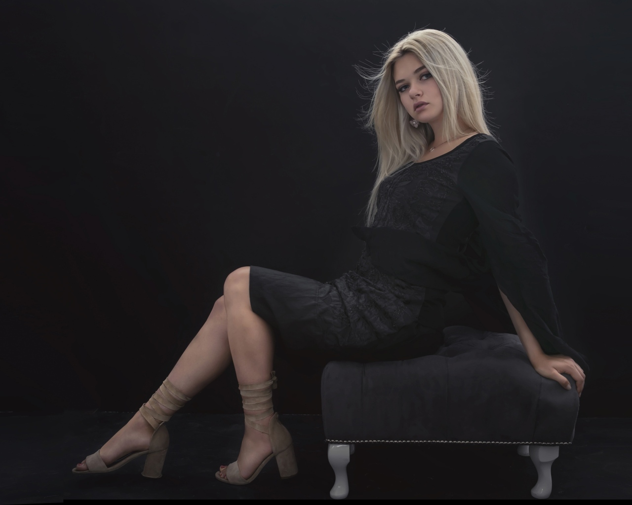 Красивая девушка в черном платье сидит на кресле