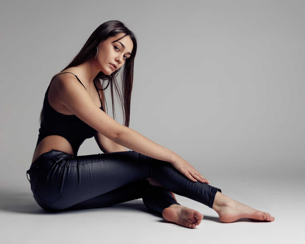 Красивая девушка в черных брюках на сером фоне